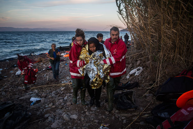 Voluntários ajudam mulher que chega em barco de refugiados à ilha de Lesbos, na Grécia (Foto: Santi Palacios/AP)
